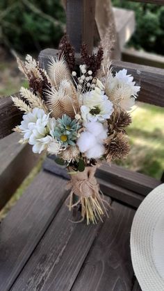 a bouquet of flowers sitting on top of a wooden bench next to a white hat