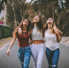 three young women walking down the street with their arms around each other and laughing together