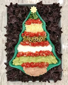 a christmas tree shaped platter with guacamole, tomatoes and olives