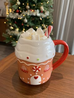 there is a coffee cup with marshmallows in it on the table next to a christmas tree