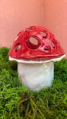 a red and white mushroom sitting on top of green grass next to a pink wall