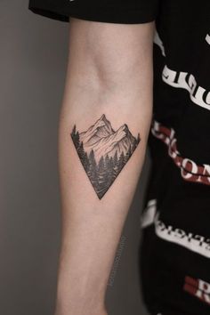 a man's arm with a tattoo on it that has mountains and trees in the background