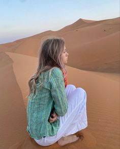 a woman sitting on top of a sandy dune