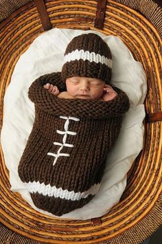 a baby wrapped in a knitted football blanket and wearing a brown hat with white stripes