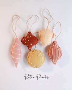 four ornaments hanging from strings on a white background with the words kite pinks written below them