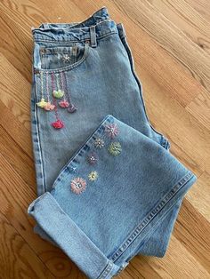 two pairs of jeans with embroidered flowers on them sitting on the floor next to each other