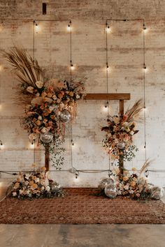 an arrangement of flowers and greenery in front of a brick wall with string lights