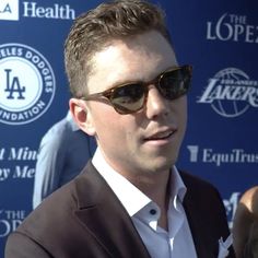 a man wearing sunglasses standing in front of a blue wall with the los angeles lakers logo on it