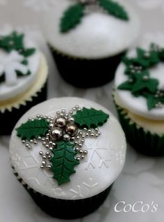 four cupcakes decorated with green and white frosting, holly leaves and beads