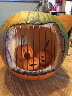 two pumpkins in a cage with faces carved into the top and sides, sitting on a table