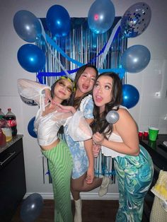 three women posing for the camera in front of balloons and streamers