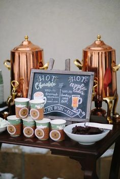 a table topped with coffee cups next to a chalkboard sign that says hot chocolate