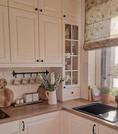 a kitchen with white cabinets and wooden counter tops next to a window that has flowers on it