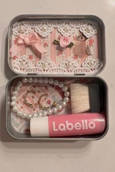 an open tin with some items inside of it on a white counter top next to a tube of lip gloss