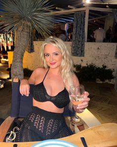 a woman sitting at a table with a glass of wine in her hand and palm tree in the background