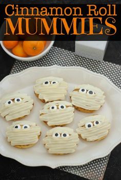 cookies decorated with icing and eyes on a plate next to an orange bowl filled with oranges