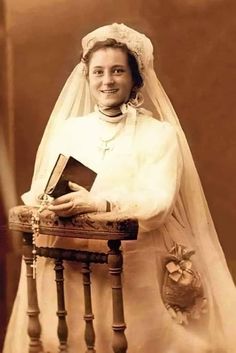 an old photo of a woman in her wedding dress holding a book and smiling at the camera