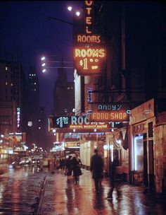 people are walking down the street in the rain at night with umbrellas and neon signs