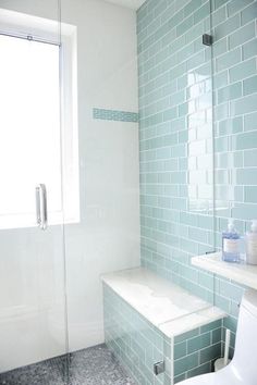 a white toilet sitting next to a window in a bathroom with blue tiles on the walls