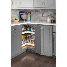 an open cabinet in the corner of a kitchen with gray cabinets and white counter tops