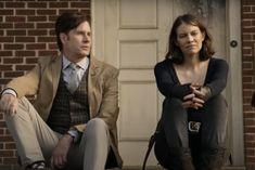 a man and woman sitting on the ground in front of a brick building with doors