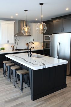 Modern kitchen with a large marble island, black cabinets, stainless steel appliances, and pendant lights. Kitchen Ideas Black Hardware, Dark Grey And White Kitchen, White And Black Kitchen Decor, Black And White Marble Kitchen, White Kitchen With Black Island, Kitchen Black Marble, Kitchen With White Countertops, White Kitchen Decor Ideas, Modern Black And White Kitchen