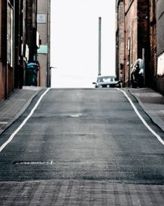 an empty street with cars parked on both sides and no one in the distance walking down it