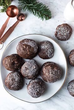 a white plate topped with chocolate donuts covered in powdered sugar