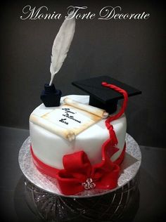 a graduation cake with a feather quill and diploma cap on top, sitting on a glass plate