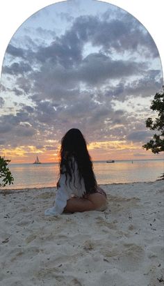 a woman sitting on top of a sandy beach next to the ocean under a cloudy sky