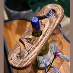 two wine glasses and a bottle on a wooden tray with flowers in the background,