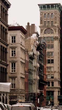 a city street filled with lots of tall buildings next to parked cars and traffic lights