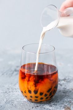 someone pouring milk into a glass filled with liquid