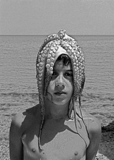 black and white photograph of a man with an octopus headdress on the beach