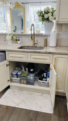 an open cabinet in the middle of a kitchen with white cabinets and marble counter tops