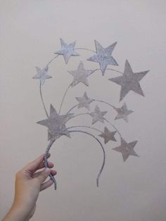 a hand is holding some silver stars on a white wall and it looks like they have been made out of tinsel