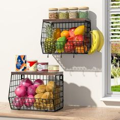 two metal baskets filled with fruits and vegetables on top of a wooden counter next to a window