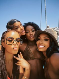 three beautiful women posing for the camera in front of a sail boat with one holding her finger up