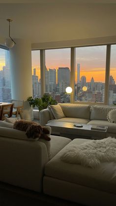 a living room filled with furniture and large windows overlooking the cityscape at sunset