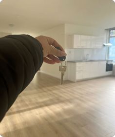 a hand holding a house key in front of a living room with white cabinets and an open kitchen