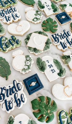 decorated wedding cookies on a table with palm leaves and monogrammed cookie cutters