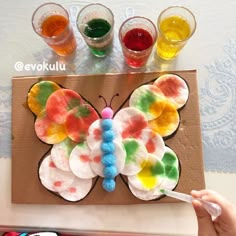 a child's hand is holding a paper plate with a butterfly on it and four glasses in the background