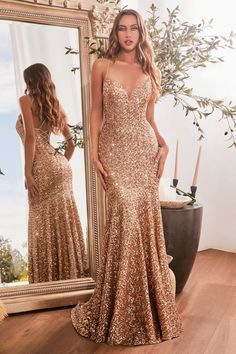 a woman standing in front of a mirror wearing a gold sequin gown with spaghetti straps