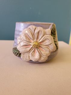 a ceramic flower ring sitting on top of a white table next to a blue wall