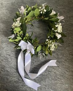 a wreath with white flowers and greenery tied around it on a gray table top