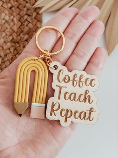 a hand holding a wooden keychain that says coffee teach repeat with a pencil in it