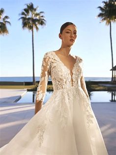 a woman in a white wedding dress standing next to palm trees and looking off into the distance