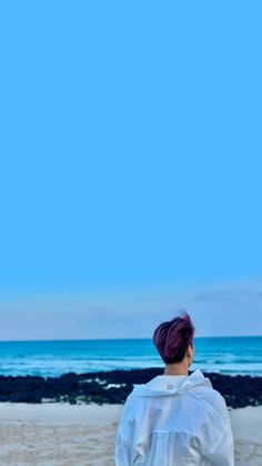 a woman standing on top of a sandy beach next to the ocean under a blue sky