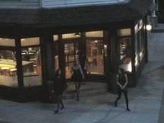 three women are walking down the sidewalk in front of a store at night, with their arms around each other