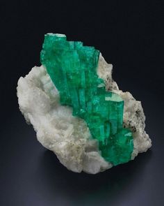 two green crystals sitting on top of a white rock